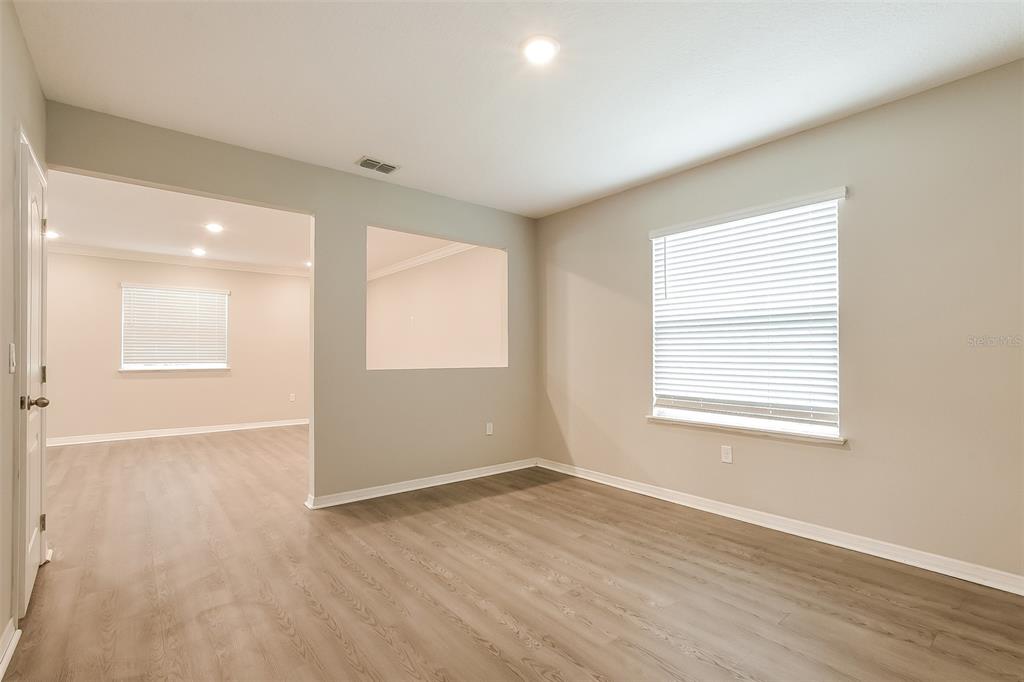 An empty room with light wood-look flooring, beige walls, and a large wall cutout — 1926 BELL CREEK LOOP, FRUITLAND PARK, FL