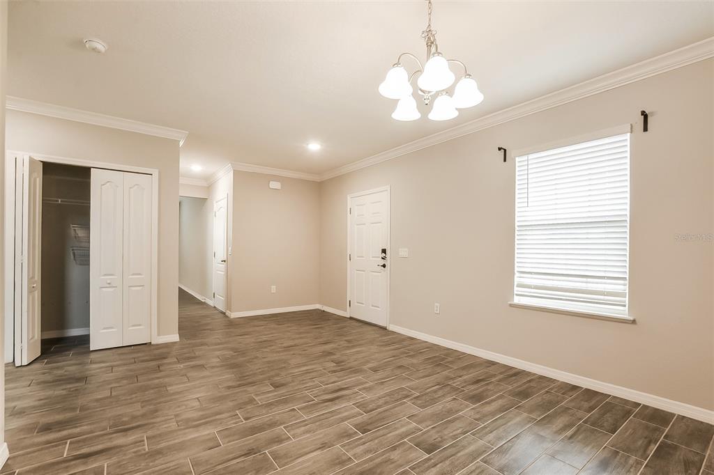 A room with wood-look tile flooring, a white chandelier, and a closet with folding doors — 1926 BELL CREEK LOOP, FRUITLAND PARK, FL