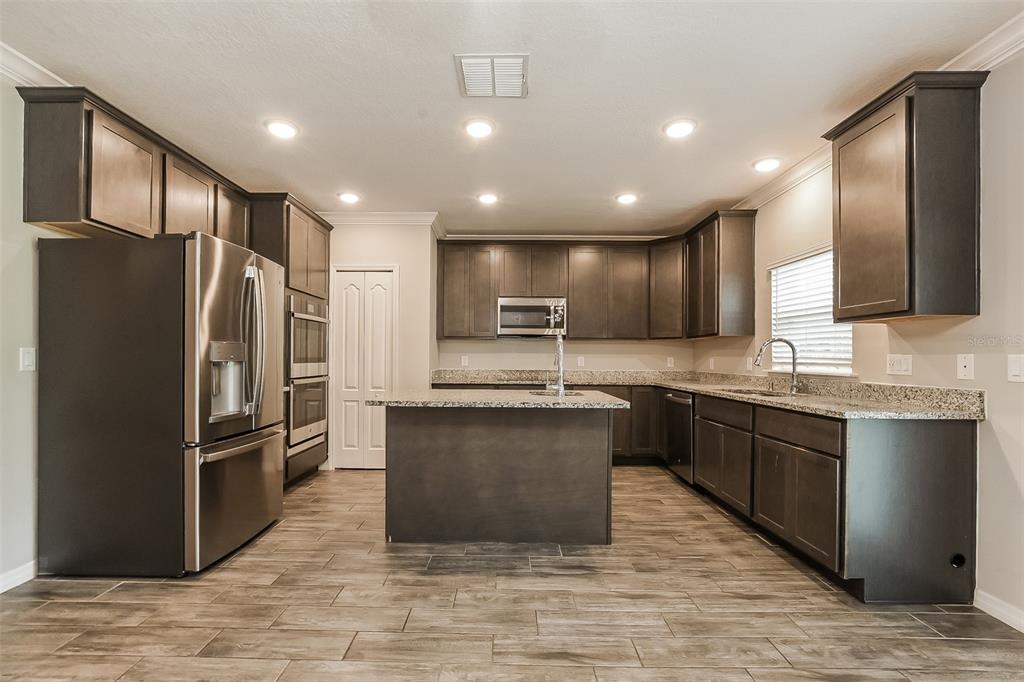 A kitchen with dark wood cabinets, stainless steel appliances, a center island, and tile flooring — 1926 BELL CREEK LOOP, FRUITLAND PARK, FL
