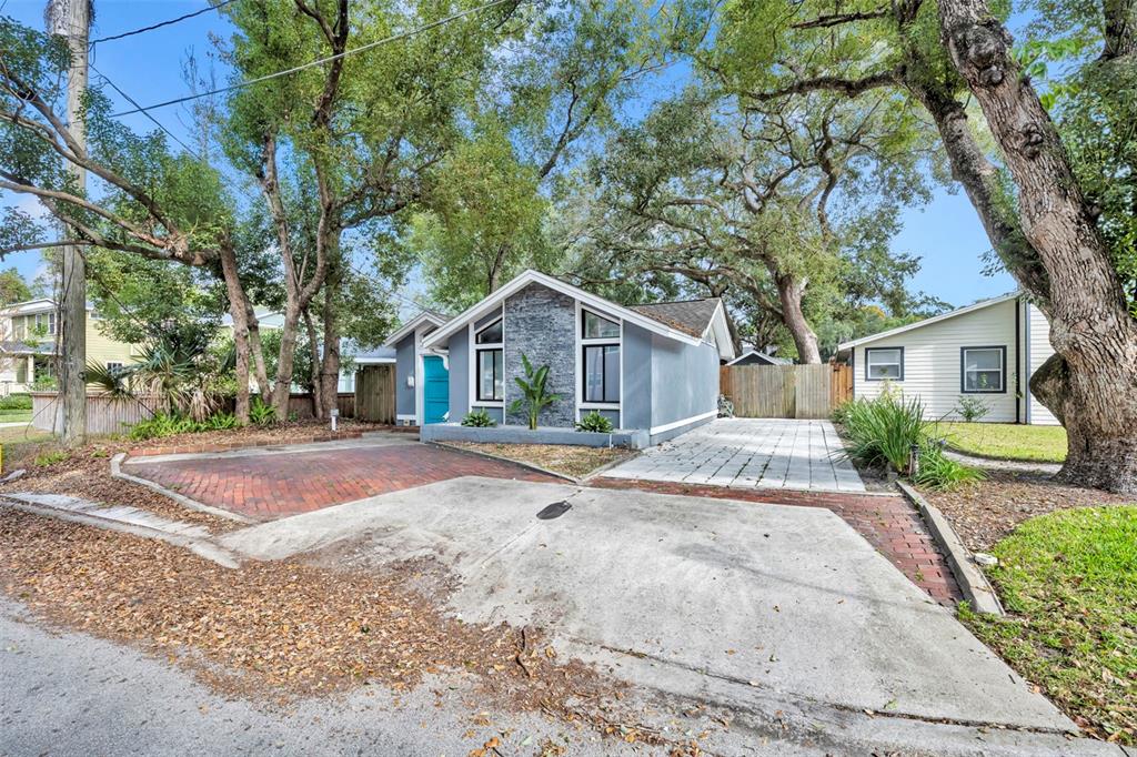 A gray house with a stone facade, brick driveway, and paved parking area under trees — 817 ALTALOMA AVENUE, ORLANDO, FL