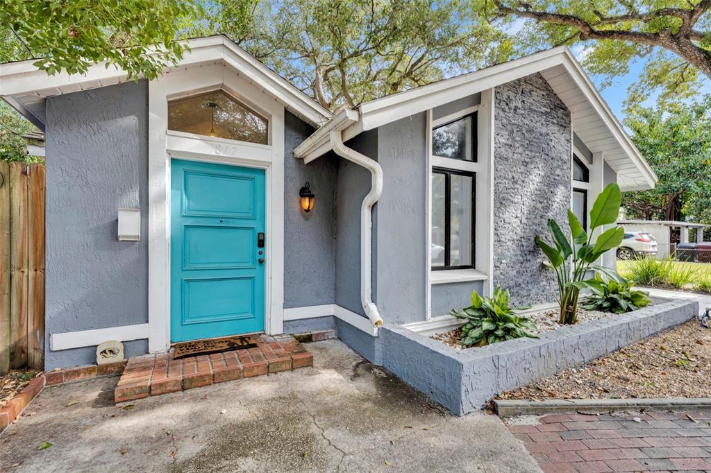 A gray house exterior features a bright teal front door and a stone-accented wall — 817 ALTALOMA AVENUE, ORLANDO, FL