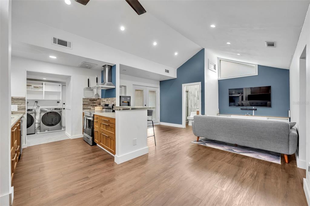 An open-concept living room and kitchen featuring wood-look flooring, blue accent walls, and vaulted ceilings — 817 ALTALOMA AVENUE, ORLANDO, FL