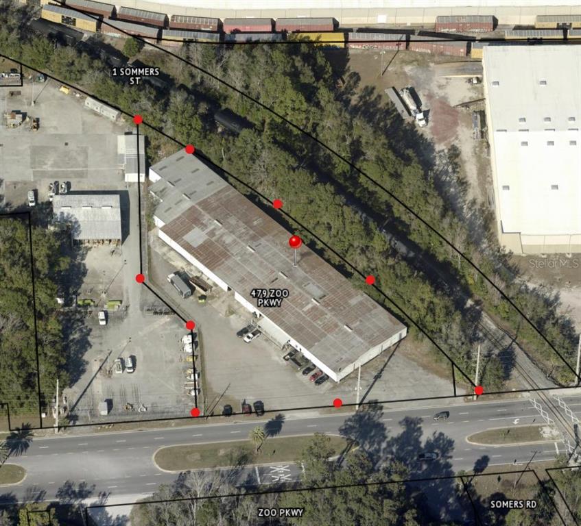 This aerial view shows an industrial building with a parking lot and surrounding trees — 479 ZOO PARKWAY, JACKSONVILLE, FL