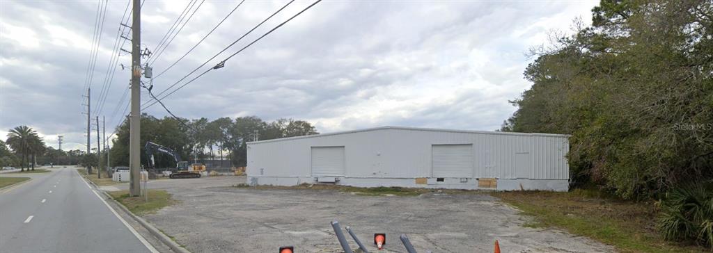A white industrial warehouse building stands next to a paved road and a wooded area — 479 ZOO PARKWAY, JACKSONVILLE, FL
