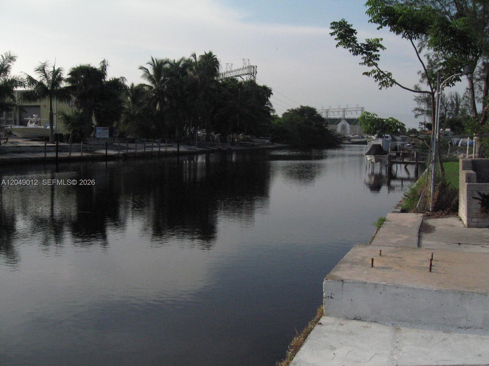 A view of a calm canal bordered by a concrete seawall, trees, and boat docks — 136 NW 14th Way, Dania Beach FL 33004, DANIA BEACH, FL