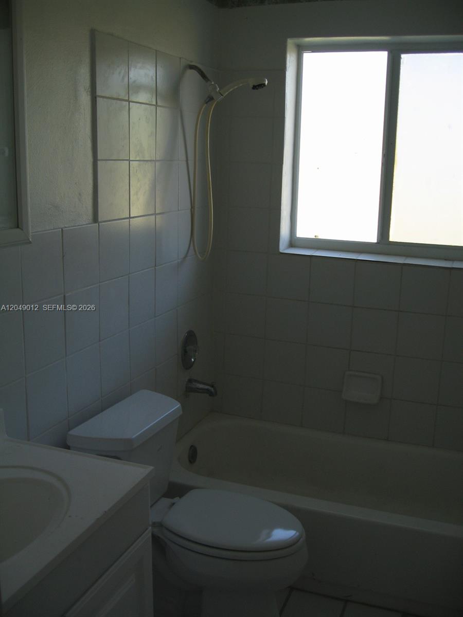 A bathroom features a white toilet, a vanity, and a bathtub with a shower head — 136 NW 14th Way, Dania Beach FL 33004, DANIA BEACH, FL