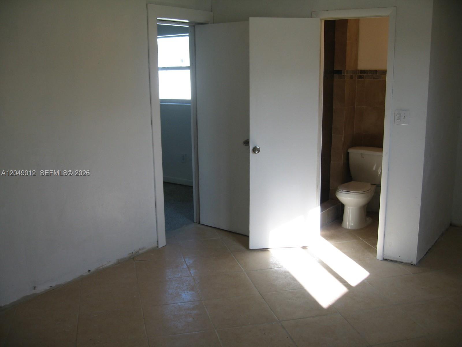 A room with tiled flooring features an open door leading to a bathroom with a toilet — 136 NW 14th Way, Dania Beach FL 33004, DANIA BEACH, FL