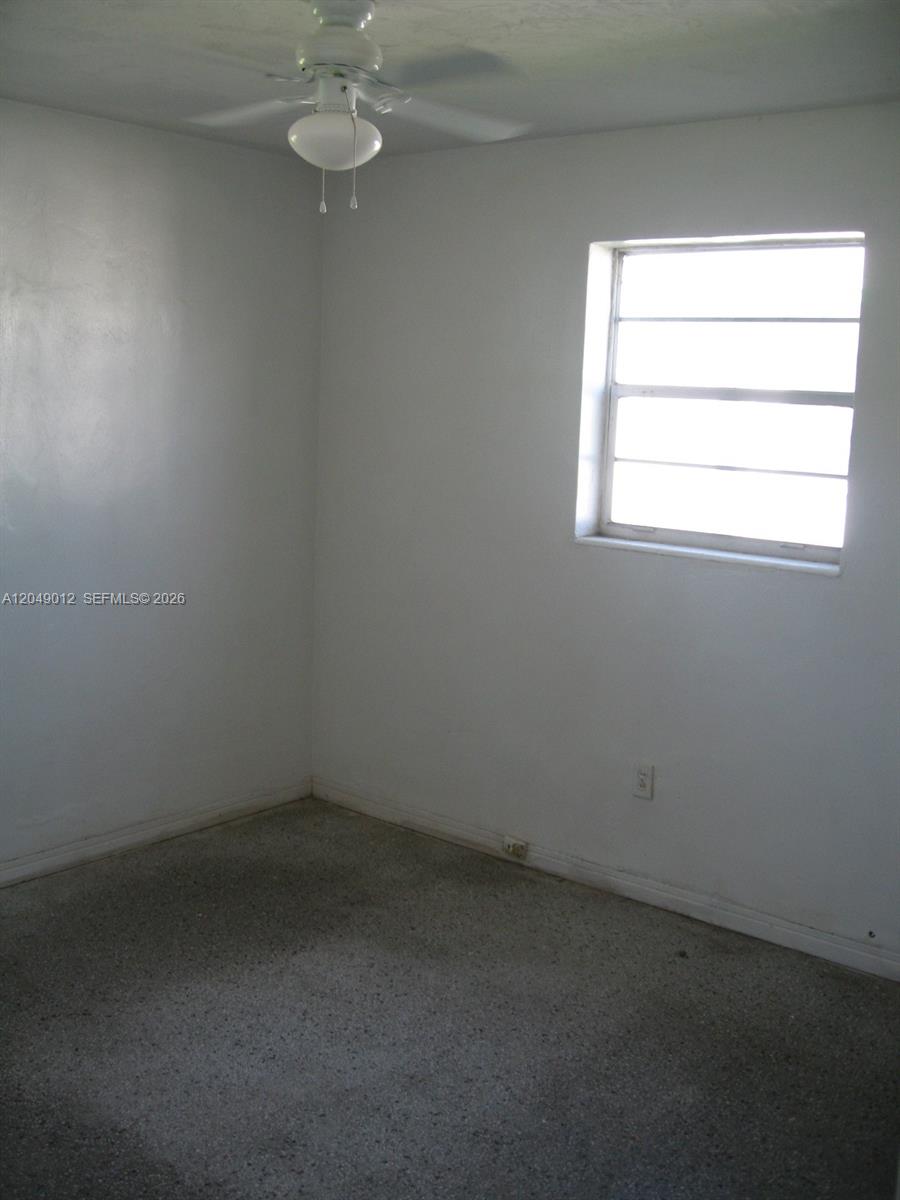 A small, empty bedroom features white walls, a ceiling fan, and gray carpeted flooring — 136 NW 14th Way, Dania Beach FL 33004, DANIA BEACH, FL