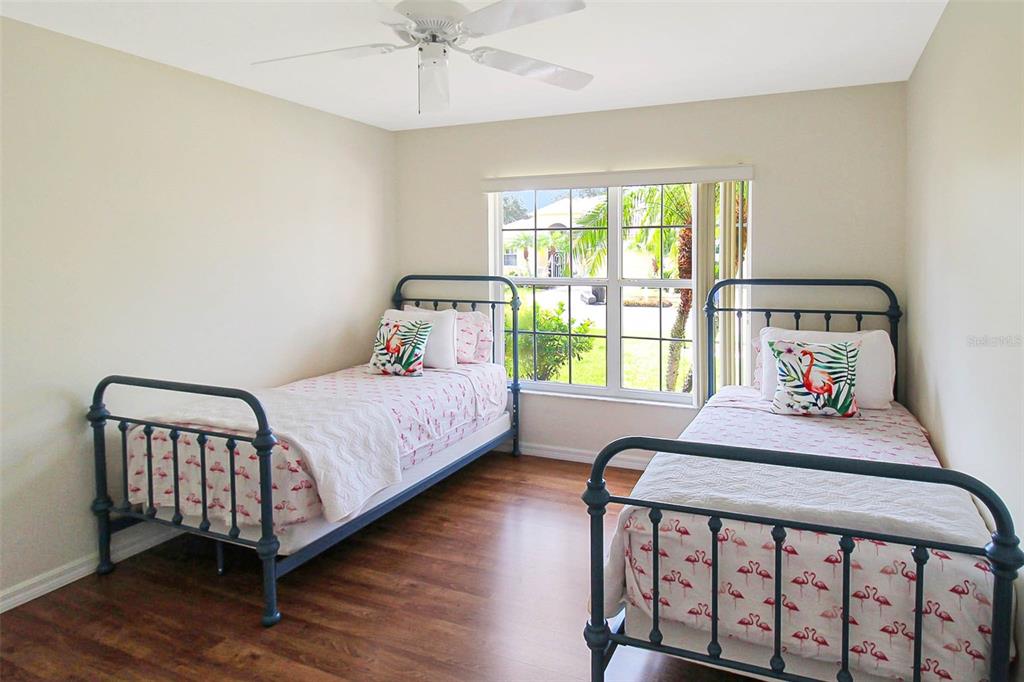 A bedroom with two twin beds, dark wood-look flooring, and a window overlooking a yard — 163 BRAEMAR AVENUE, VENICE, FL