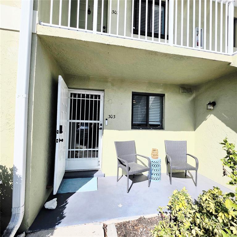 An exterior view of a ground-floor apartment entrance with a patio and two chairs — 25225 RAMPART BOULEVARD UNIT 303, PUNTA GORDA, FL