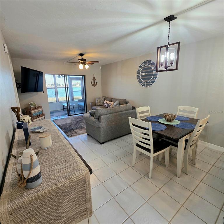 A dining area and living room with tile floors, a ceiling fan, and sliding glass doors — 25225 RAMPART BOULEVARD UNIT 303, PUNTA GORDA, FL