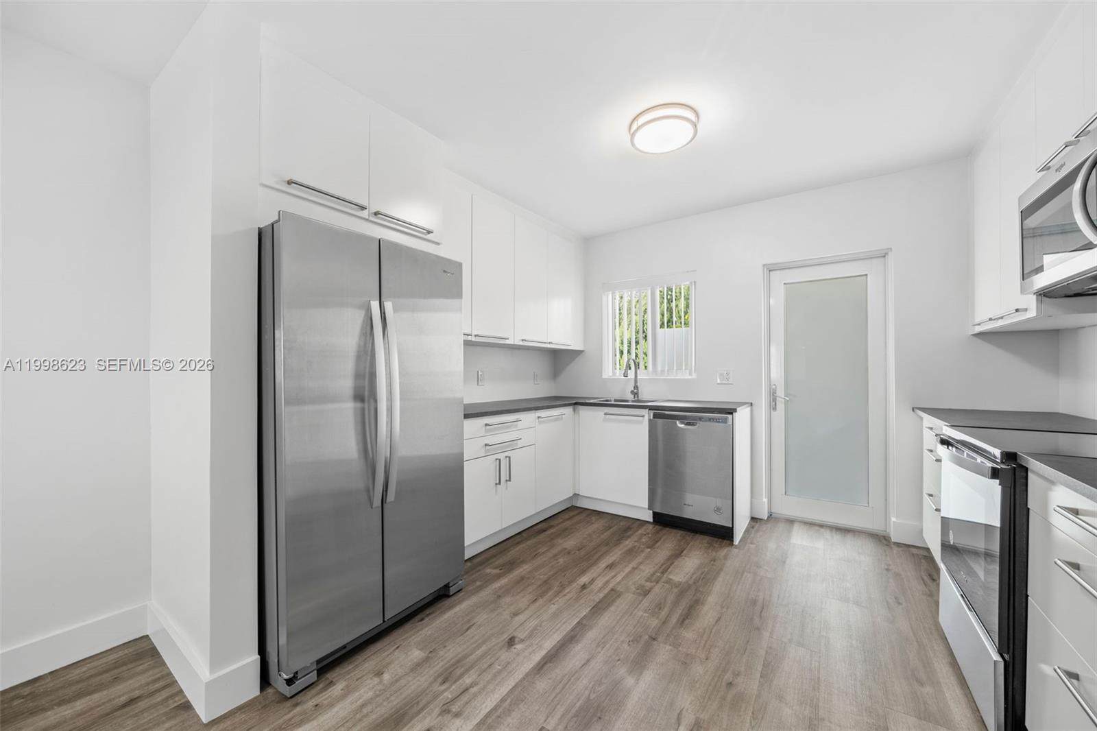 A modern kitchen features white cabinets, stainless steel appliances, and wood-look flooring — 600 Layne Blvd # 126, Hallandale Beach FL 33009, HALLANDALE BEACH, FL