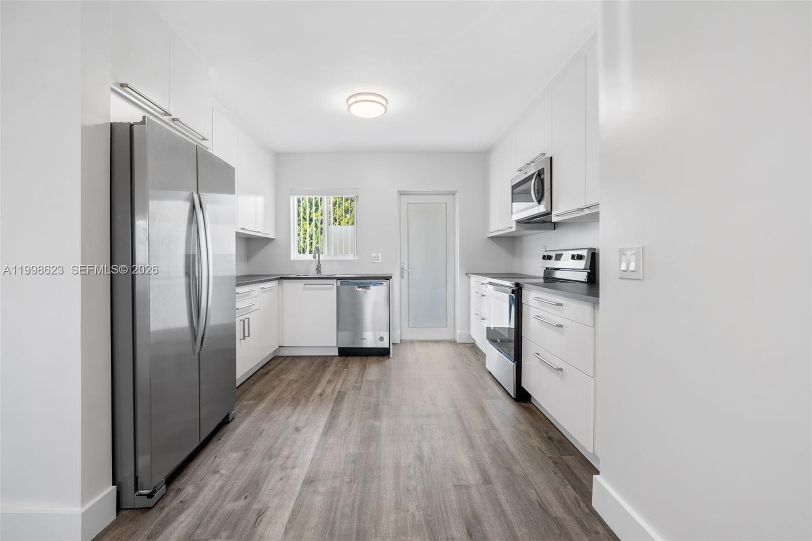 A modern kitchen features white cabinets, stainless steel appliances, and wood-look flooring — 600 Layne Blvd # 126, Hallandale Beach FL 33009, HALLANDALE BEACH, FL