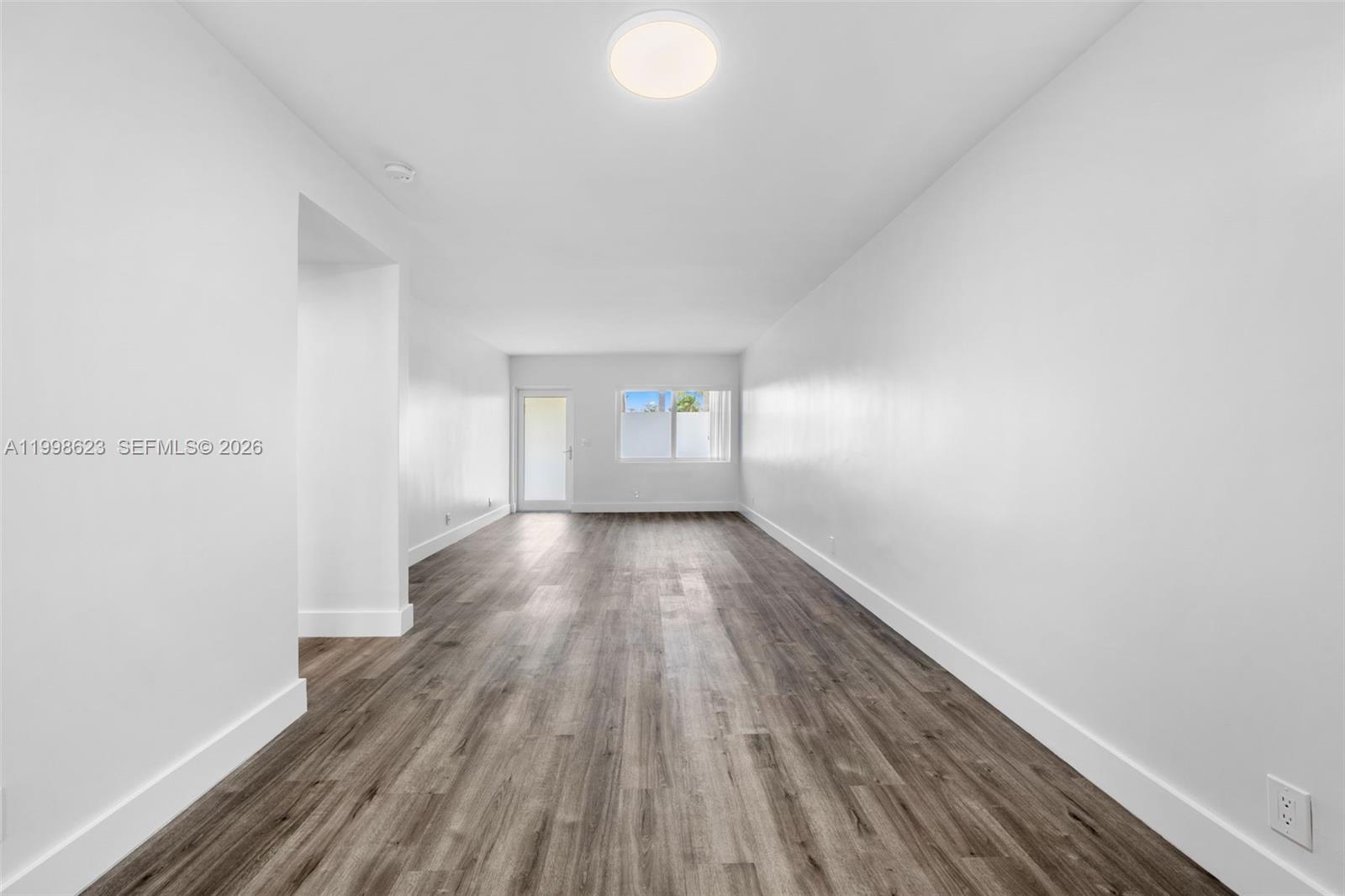An empty room features white walls, wood-look flooring, a ceiling light, and a glass door — 600 Layne Blvd # 126, Hallandale Beach FL 33009, HALLANDALE BEACH, FL