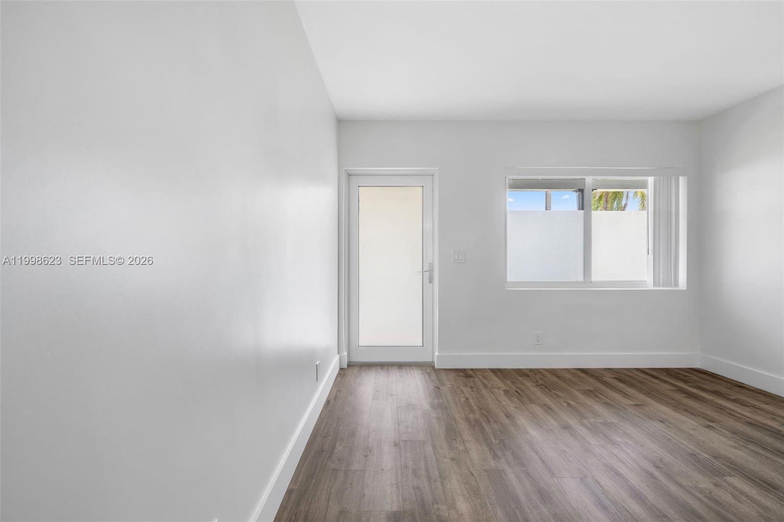 A room with white walls, wood-look flooring, a glass-paneled door, and a window — 600 Layne Blvd # 126, Hallandale Beach FL 33009, HALLANDALE BEACH, FL