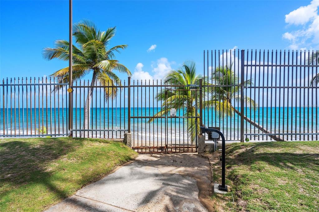 A metal gate and fence provide access to a sandy beach with palm trees — 2305 LAUREL UNIT 614, SAN JUAN, PR