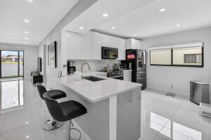A modern kitchen features white cabinetry, a quartz island with bar stools, and tiled flooring — 15401 Pembridge Avenue # 15, Delray Beach FL 33484, DELRAY BEACH, FL