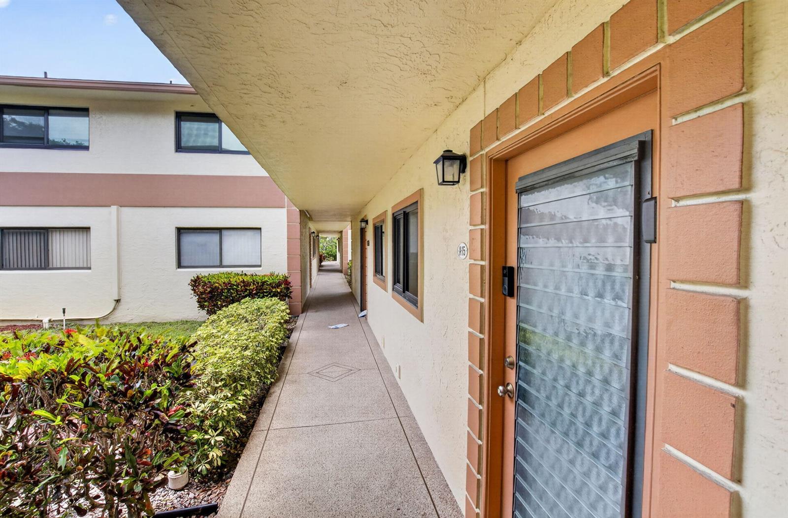 An outdoor walkway leads past apartment doors with louvered glass inserts and brick-style trim — 15401 Pembridge Avenue # 15, Delray Beach FL 33484, DELRAY BEACH, FL