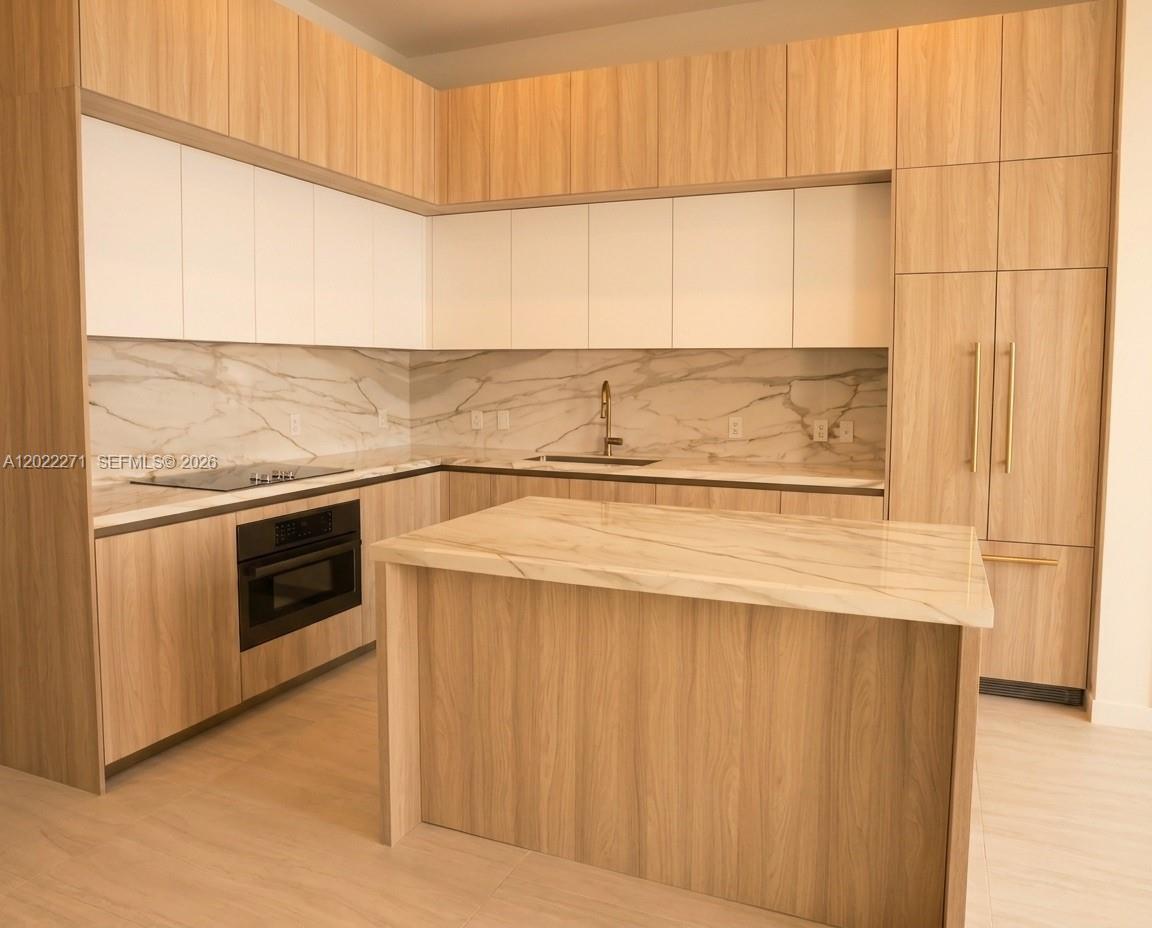 A modern kitchen features light wood cabinetry, white upper cabinets, and a marble-topped island — 77 SE 5 St, Miami FL 33131, MIAMI, FL