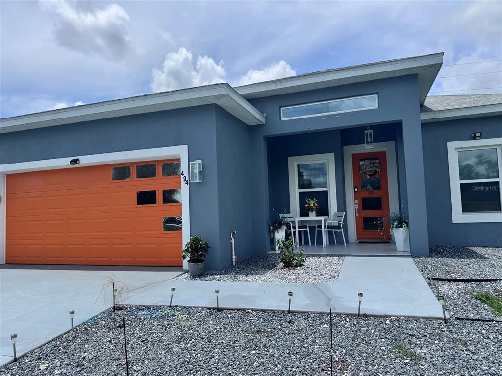 A blue house features an orange garage door, a matching front door, and a gravel yard — 494 MARION OAKS DRIVE, OCALA, FL