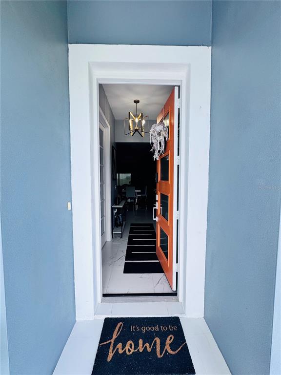 An open orange front door reveals a tiled entryway with a modern chandelier and runner — 494 MARION OAKS DRIVE, OCALA, FL