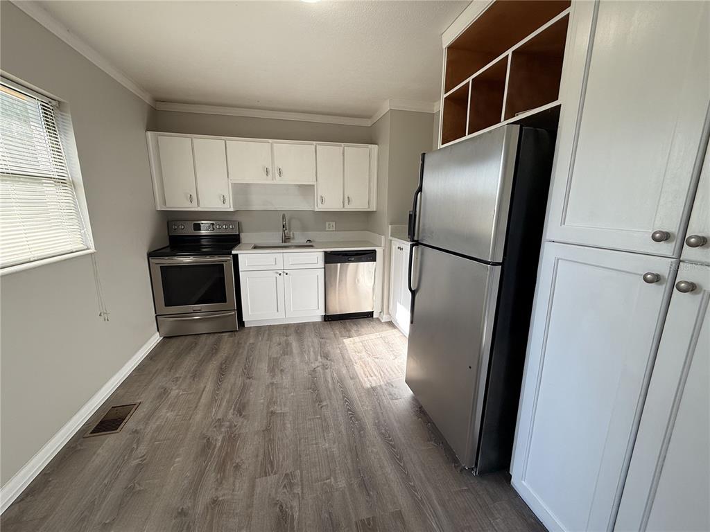 A kitchen features white cabinets, stainless steel appliances, and wood-look flooring — 307 S ORANGE AVENUE, DELAND, FL