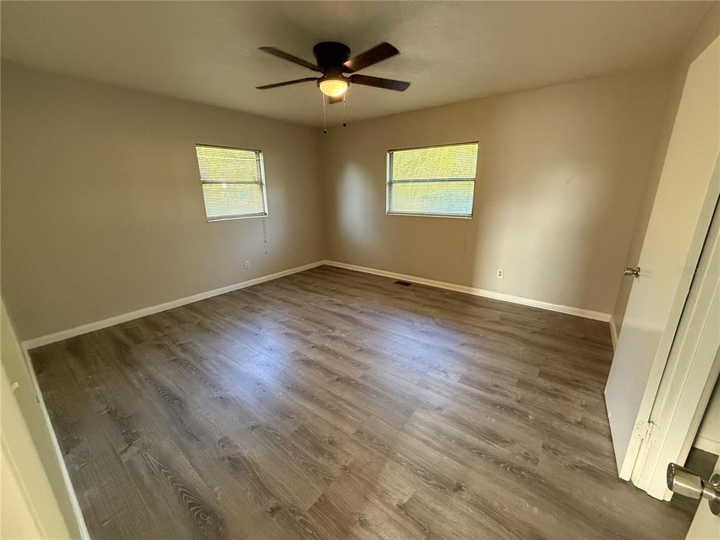 An empty bedroom features light-colored walls, wood-look flooring, two windows, and a ceiling fan — 307 S ORANGE AVENUE, DELAND, FL