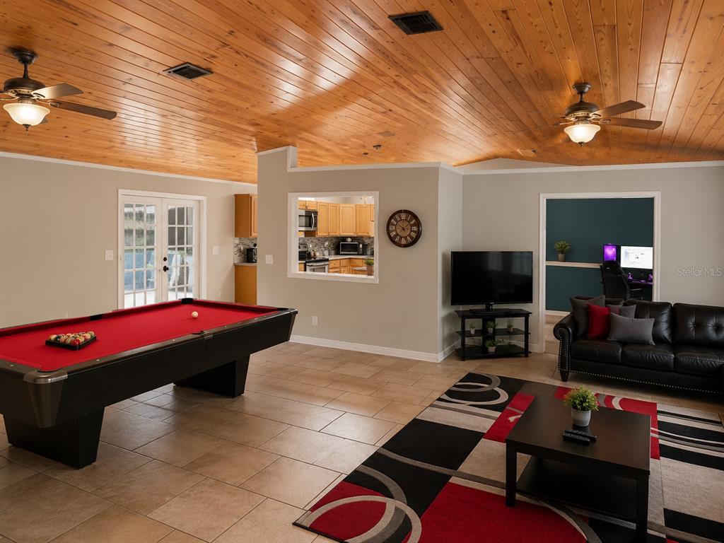 A living room with a pool table, tile floors, wood-paneled ceiling, and an open kitchen — 1292 VALLEYBROOK ROAD SE, PALM BAY, FL