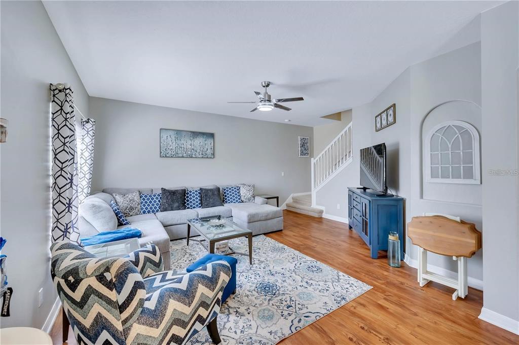 A living room features a grey sectional sofa, patterned armchair, television console, and wood flooring — 280 CAPE HARBOUR LOOP UNIT 101, BRADENTON, FL