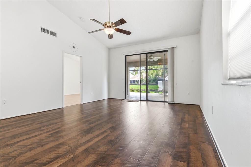 A living room with dark wood-look flooring, a ceiling fan, and sliding glass patio doors — 5515 SALEM SQUARE DRIVE S, PALM HARBOR, FL