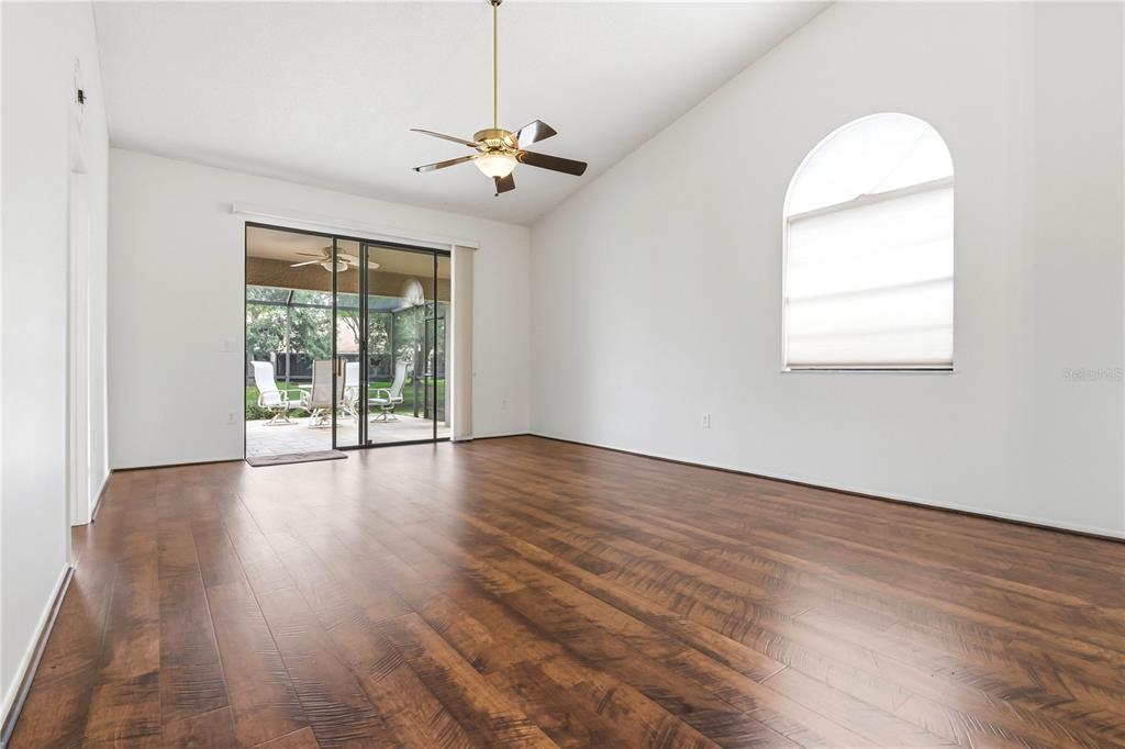 An empty living room features dark wood-look flooring, a vaulted ceiling, and a sliding glass door — 5515 SALEM SQUARE DRIVE S, PALM HARBOR, FL