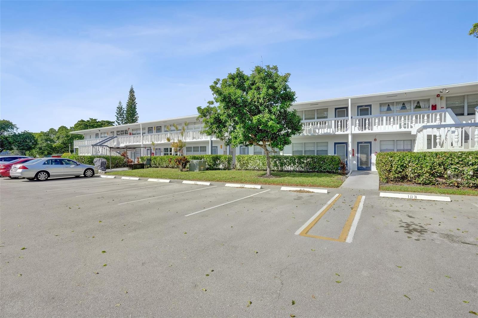 A two-story white apartment building sits behind a paved parking lot with numbered spaces — 91 Tilford, Deerfield Beach FL 33442, DEERFIELD BEACH, FL
