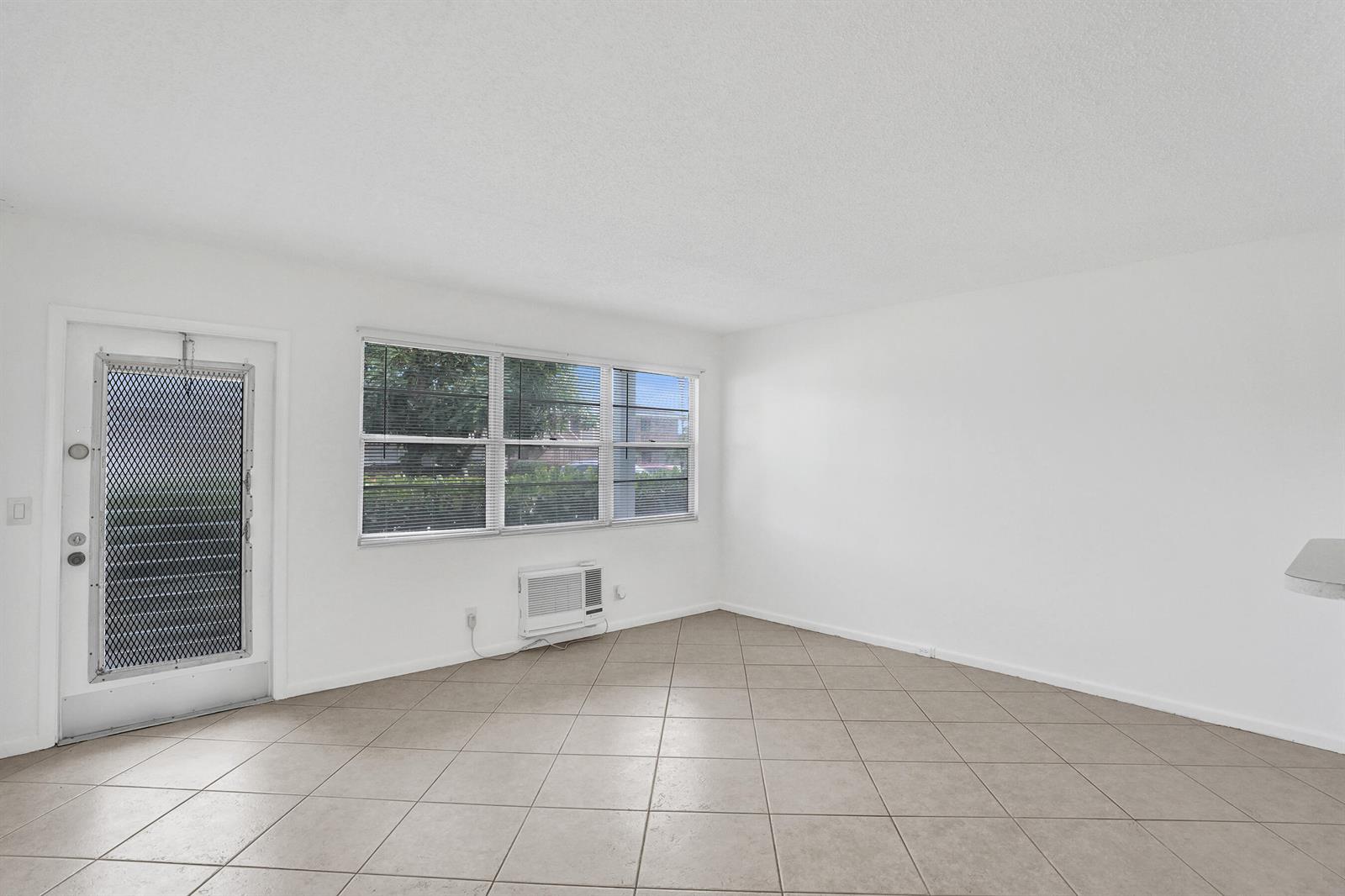 An empty room with white walls, tile flooring, a window, and a door with a screen — 91 Tilford, Deerfield Beach FL 33442, DEERFIELD BEACH, FL