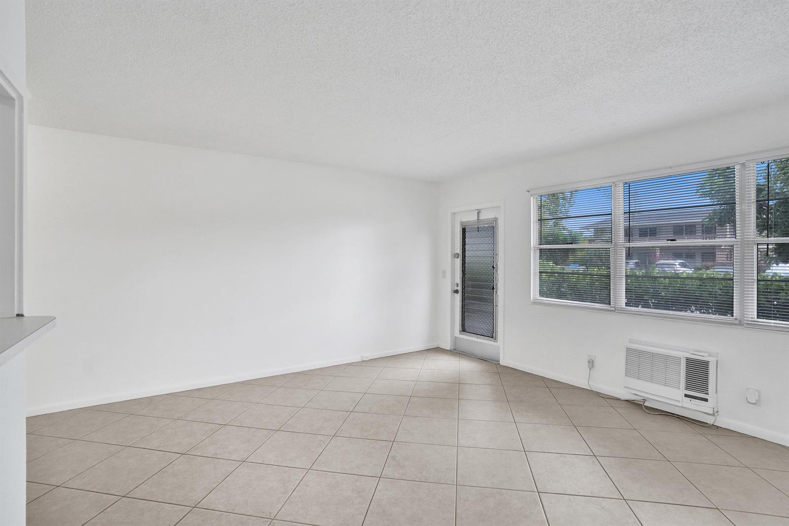 An empty living room with white walls, beige tile flooring, and a window air conditioner — 91 Tilford, Deerfield Beach FL 33442, DEERFIELD BEACH, FL