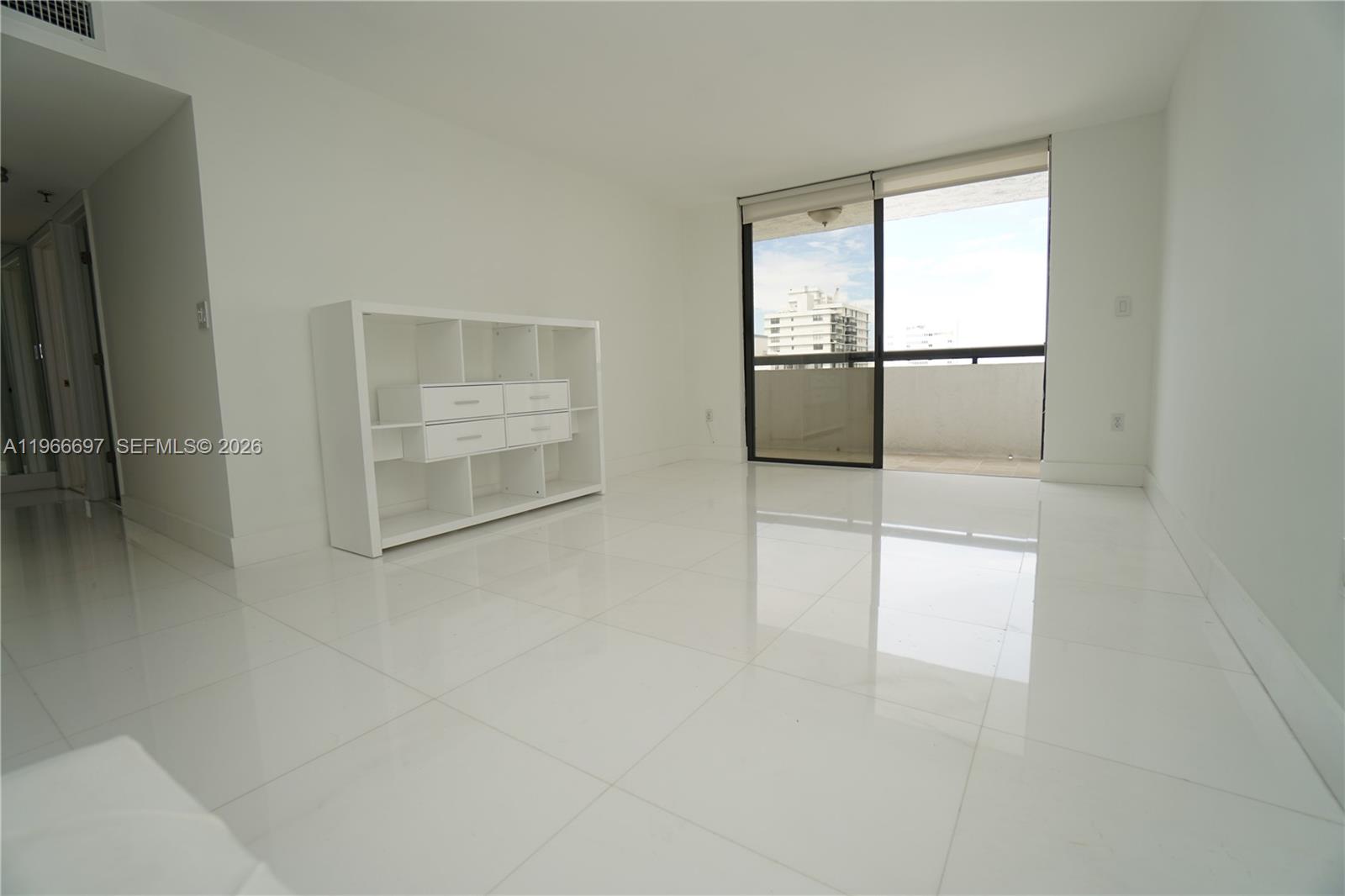 A bright, empty room features white tiled floors, a white shelving unit, and a balcony — 1775 Washington Ave # 11C, Miami Beach FL 33139, MIAMI BEACH, FL