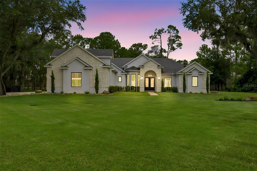 A single-story house with stone accents and a large front lawn at sunset — 13961 SMOKERISE COURT, ORLANDO, FL