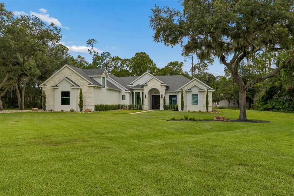 A single-story house with a white stone facade and a large green lawn — 13961 SMOKERISE COURT, ORLANDO, FL