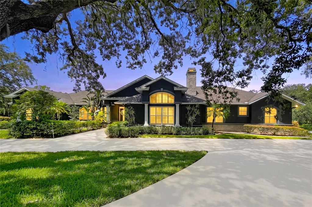 A dark-painted single-story house with a stone chimney and a large paved driveway — 2918 MAGNOLIA TRACE, TARPON SPRINGS, FL