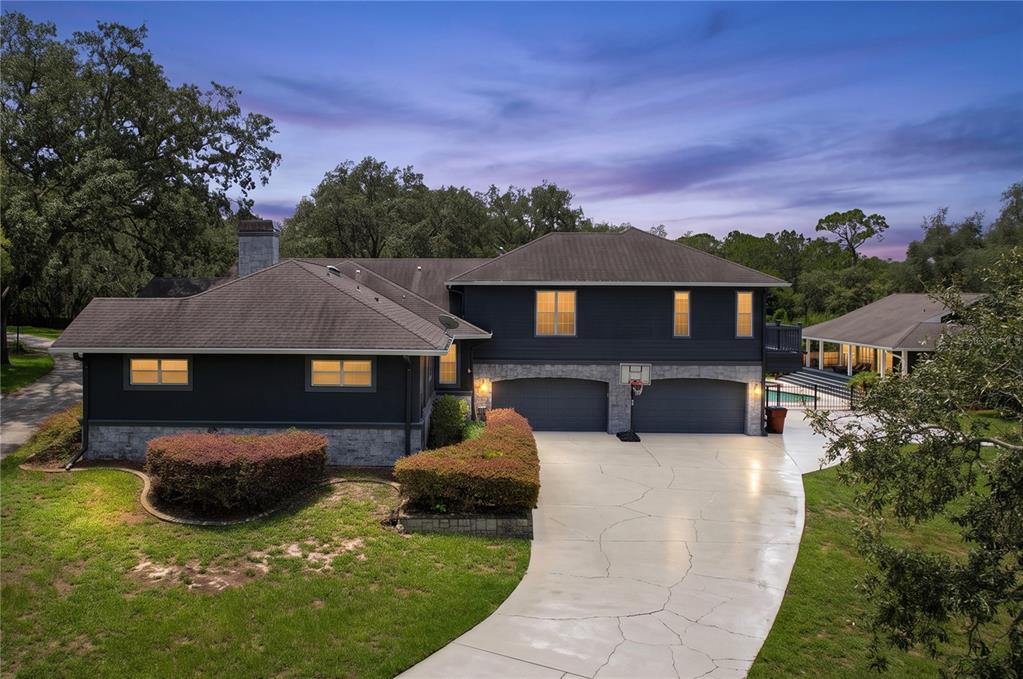 An exterior view of a dark-painted two-story house with a stone base and concrete driveway — 2918 MAGNOLIA TRACE, TARPON SPRINGS, FL