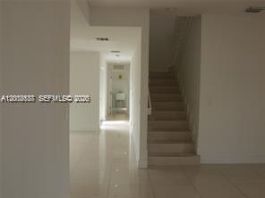 A hallway with light-colored tile flooring leads to a doorway, with a staircase on the right — 15650 SW 11th Ter # 0, Miami FL 33194, MIAMI, FL