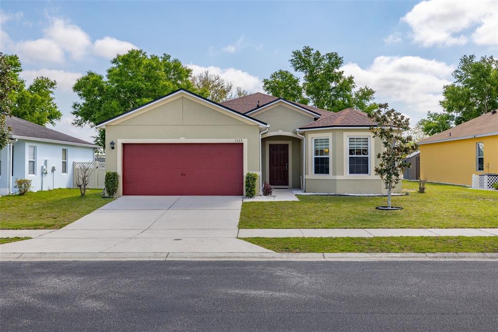 A single-story house with a red garage door, tan stucco exterior, and a front walkway — 1325 CYPRESS RIDGE LOOP, LAKE ALFRED, FL