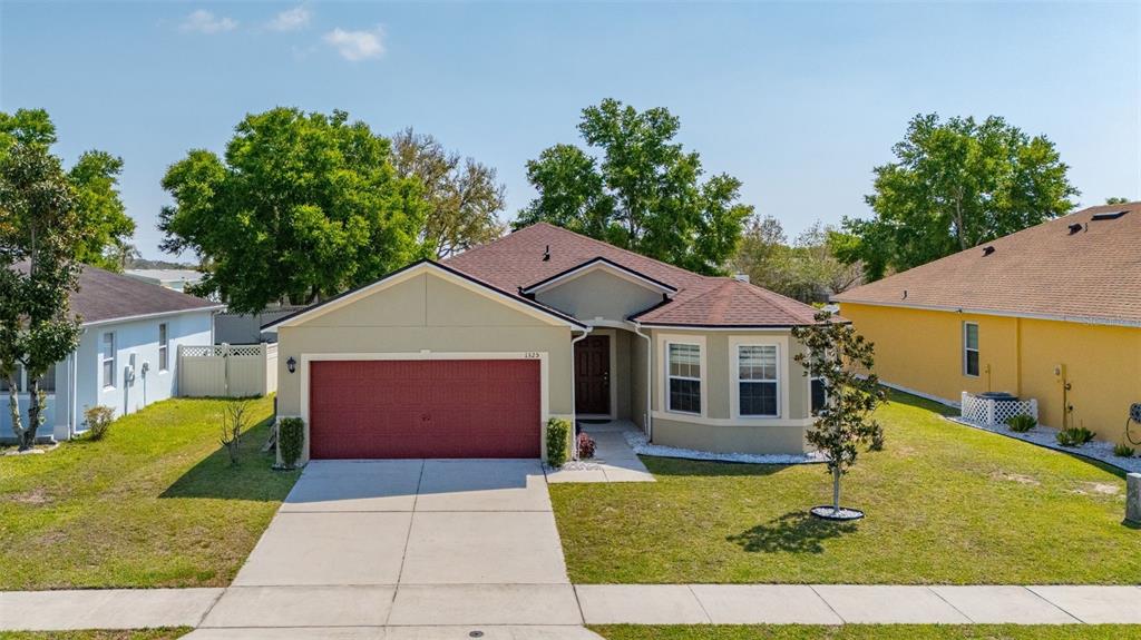 A single-story house with a red garage door, tan siding, and a brown shingled roof — 1325 CYPRESS RIDGE LOOP, LAKE ALFRED, FL