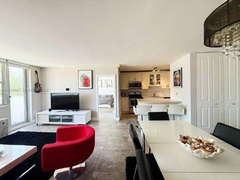 This open-concept living and dining area features tile flooring, a modern kitchen, and balcony access — MIAMI BEACH, FL