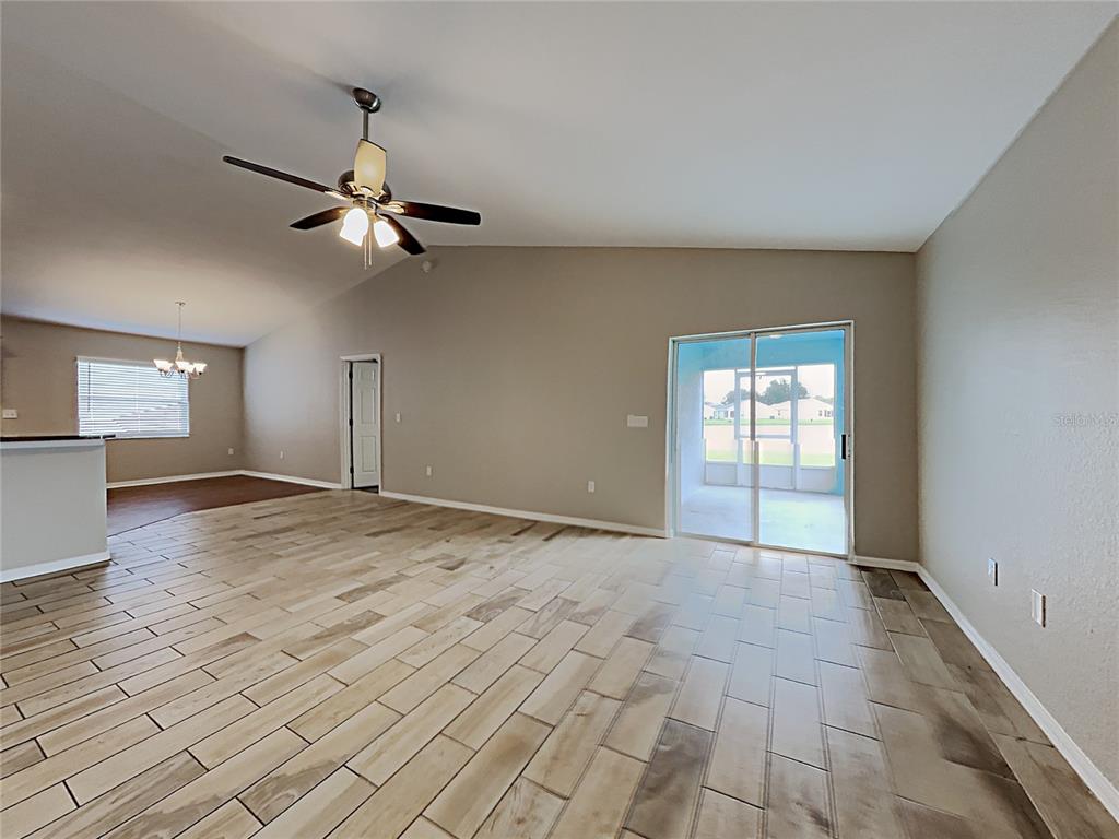 An open-concept living area features vaulted ceilings, wood-look tile flooring, and sliding glass patio doors — 3030 GRAND PRESERVE BOULEVARD, MULBERRY, FL