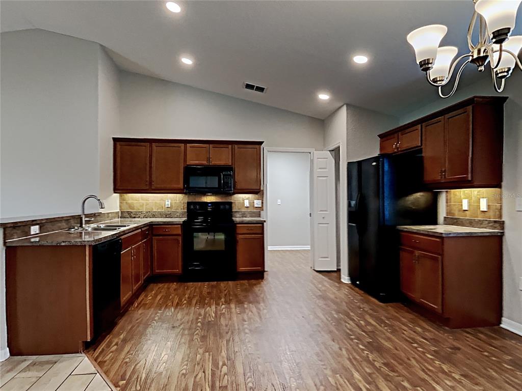 A kitchen features dark wood cabinets, black appliances, laminate countertops, and wood-look flooring — 3030 GRAND PRESERVE BOULEVARD, MULBERRY, FL