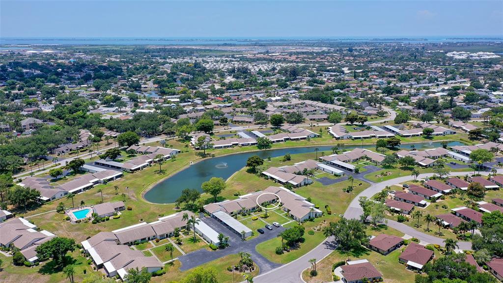 An aerial view shows a residential community with single-story buildings, a central pond, and landscaping — 6129 HERITAGE LANE W UNIT 6129, BRADENTON, FL