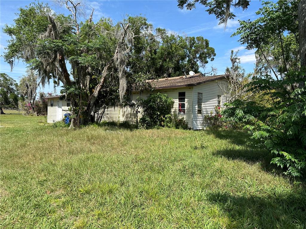 A single-story house with light-colored siding sits in a grassy yard surrounded by trees — 4090 CARLTON ROAD, SARASOTA, FL