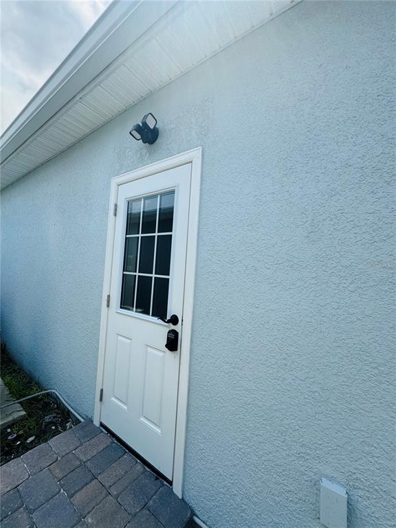 A white exterior door with a window is set into a light blue stucco wall — 1433 GRAND PALM DRIVE, ORLANDO, FL