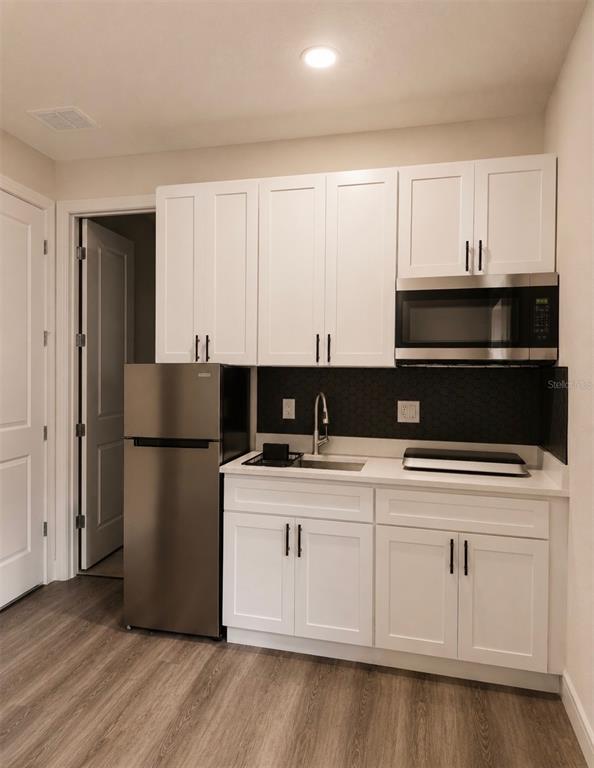 A small kitchenette features white cabinets, stainless steel appliances, and a dark backsplash — 1433 GRAND PALM DRIVE, ORLANDO, FL