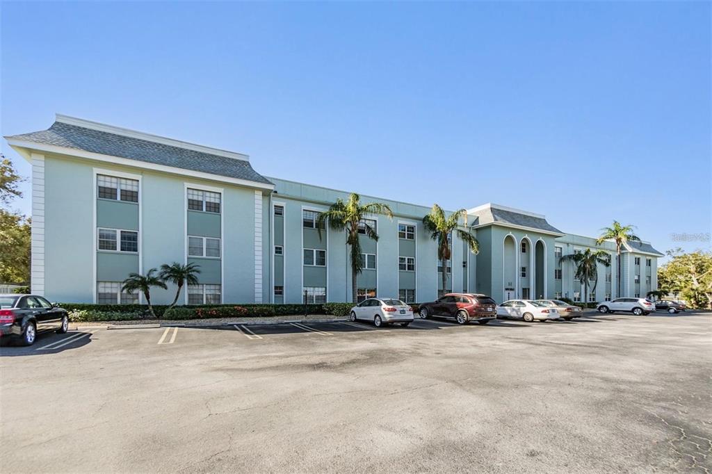 A multi-story, light green apartment building with a parking lot in the foreground — 1706 BELLEAIR FOREST DRIVE UNIT 136, CLEARWATER, FL